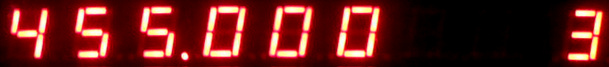 Dieser Alt-Text wurde noch nicht überprüft.
<p>Zusammenfassung: Eine rote Siebensegmentanzeige auf schwarzem Hintergrund zeigt die Zahlenfolge 455.000, rechts ist eine weitere, angeschnittene Ziffer zu sehen.</p>
<p>Detailbeschreibung: Das Bild ist ein schmaler, horizontaler Ausschnitt einer digital leuchtenden Anzeige mit roten Siebensegmentziffern vor schwarzem Hintergrund. Von links nach rechts sind deutlich die Ziffern 4, 5, 5 zu sehen, gefolgt von einem leuchtenden Dezimalpunkt und drei Nullen (0 0 0). Die Segmente strahlen leicht über, wodurch ein weicher roter Glanz um die Balken entsteht. Am rechten Bildrand ist der linke Teil einer weiteren Ziffer angeschnitten, deren Form nicht vollständig erkennbar ist.">
<figcaption>Abbildung NEA-13.29.1: Display eines Frequenzzählers, der $\qty{455}\cdot 10^3 Hz$ anzeigt</figcaption></p>
</figure>
</aside>
<aside class=