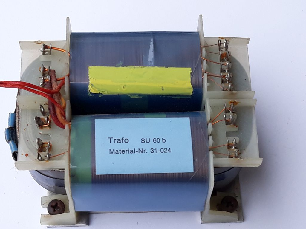 Dieser Alt-Text wurde noch nicht überprüft.
<p>Kurzbeschreibung: Ein Transformator mit zwei Wicklungen und seitlichen Anschlussleisten, von oben auf weißem Hintergrund fotografiert.</p>
<p>Detaillierte Beschreibung: Das Gerät besteht aus einem rechteckigen Blechkern mit zwei nebeneinander liegenden Spulenkörpern, die mit blaugrünem Isoliermaterial umwickelt sind. Auf der oberen Spule klebt mittig ein gelber Streifen, auf der unteren Spule ein hellblaues Etikett mit der Aufschrift „Trafo  SU 60 b“ und „Material-Nr. 31-024“. An beiden Stirnseiten befinden sich helle Kunststoffträger mit Reihen von metallischen Lötfahnen; daran sind feine, lackierte Kupferdrähte angeschlossen, teils mit sichtbaren Lötstellen und leichten Anlaufspuren. Links führen zwei rote flexible Leitungen zu einer Anschlussseite; daneben ist ein kleines blaues zylindrisches Element zu sehen. Unten sind Montagewinkel mit Schrauben erkennbar. Der Hintergrund ist einheitlich weiß, das Foto zeigt das Bauteil leicht von oben.">
<figcaption>Abbildung NEA-8.6.2: Trafo mit sichtbar getrennten Wicklungen</figcaption></p>
</figure>
</aside>
Ein Transformator dient zur Umsetzung einer hohen Wechselspannung z. B. $230&nbsp;V$ in eine 
niedrigere Wechselspannung z. B. $13,8&nbsp;V$. Ein Transformator kann nur Wechselspannungen übertragen. Legt man unerlaubt eine Gleichspannung an einen Transformator an, wirkt dieser aufgrund des geringen ohmschen Widerstands der Primärwicklung wie ein Kurzschluss. Der Transformator kann dadurch stark überhitzen und im schlimmsten Fall durchbrennen.
<hr />
<p>Das Übersetzungsverhältnis eines Transformators lässt sich wie folgt angeben:</p>
<p>$ü = \frac{N_P}{N_S} = \frac{U_P}{U_S}$</p>
<p>Das Verhältnis der Windungszahlen entspricht somit dem Verhältnis der Spannungen. Durch Umstellen dieser Grundgleichung lassen sich sowohl die Spannungen $U$ als auch die Windungszahlen $N$ auf der Primär- oder Sekundärseite berechnen.</p>
<aside class=