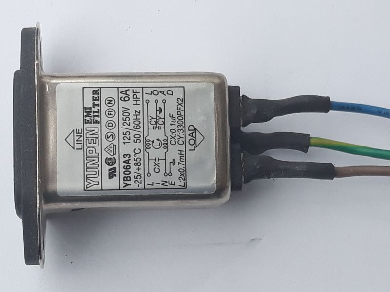Dieser Alt-Text wurde noch nicht überprüft.
<ol>
<li>
<p>Kurze Zusammenfassung: Ein rechteckiges EMI‑Filter im Metallgehäuse mit Typenschild liegt auf weißem Hintergrund; rechts führen drei isolierte Adern (blau, gelb‑grün, braun) aus dem Gerät.</p>
</li>
<li>
<p>Detaillierte Beschreibung: Das silbern glänzende, rechteckige Gehäuse hat links einen schwarzen Montageflansch; auf der Oberseite befindet sich ein Etikett mit der Aufschrift „YUNPEN EMI FILTER“, Modell „YB06A3“, Nennwerten „6A“, „125/250V“, „50/60Hz“, Temperaturbereich „−25 bis +85°C“ sowie mehreren Prüf- und Zulassungszeichen. Ein Pfeil mit „LINE“ zeigt zum Flansch, ein Pfeil mit „LOAD“ nach rechts. Auf dem Etikett ist ein Schaltbild mit Bauteilangaben zu sehen, darunter „Lx: 2×0.7mH“, „Cx: 0.1µF“, „Cy: 2×3300pF X2“, mit Anschlusskennzeichnungen L, N und Erde-Symbol. Rechts treten drei Adern aus dem Gehäuse aus, jeweils mit schwarzem Schrumpfschlauch am Austritt; die Adern sind von oben nach unten blau, gelb‑grün und braun und verlaufen leicht nach rechts. Das Metall zeigt kleine Kratzer und matte Stellen; der Hintergrund ist eine glatte, weiße Fläche."></p>
 <figcaption>Abbildung EA-11.12.1: Netzfilter</figcaption>
</li>
</ol>
</figure>
<figure class=