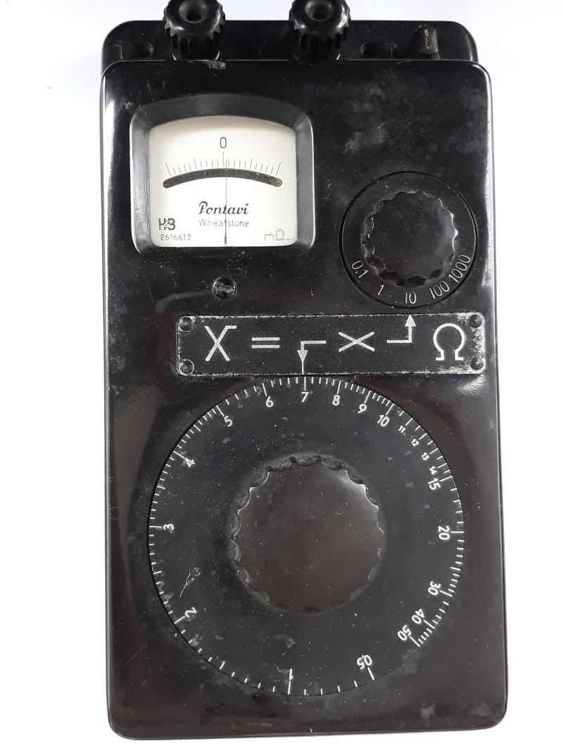 Dieser Alt-Text wurde noch nicht überprüft.
<ol>
<li>
<p>Kurze Zusammenfassung: Schwarzes Messgerät mit analogem Zeigerinstrument, großem Drehring, zusätzlichem Drehschalter und mehreren Anschlussklemmen.</p>
</li>
<li>
<p>Detaillierte Beschreibung: Das Gerät hat ein rechteckiges, schwarzes Gehäuse und liegt auf weißem Untergrund. Oben links befindet sich ein rechteckiges Analoginstrument mit gebogener Skala und der mittigen Markierung „0“; auf der Skalenfläche steht „Pontavi Wheatstone“ sowie ein Ω-Symbol. Oben am Rand sitzen zwei schwarze Schraubklemmen; rechts oben sind zwei kleine, stiftartige Anschlüsse zu sehen. Rechts neben dem Messwerk ist ein kleinerer Drehschalter mit Skalenring, beschriftet mit 0,1 – 1 – 10 – 100 – 1000. Unterhalb des Messwerks ist eine schmale Metallplakette mit der Aufschrift „X =“ und Symbolen sowie einem Ω-Zeichen verschraubt. Den unteren Bereich dominiert ein großer, runder Drehring mit feiner Teilung und Zahlen von 0 bis 50 (in 5er-Schritten markiert), in dessen Mitte ein griffig ausgeformter Drehknauf sitzt. Das Gehäuse zeigt leichte Kratzer und Gebrauchsspuren; mehrere Schrauben sind sichtbar."></p>
 <figcaption>Abbildung NEA-9.6.2: Widerstandsmessbrücke nach Wheatstone (Pontavi)</figcaption>
</li>
</ol>
</figure>
<p>Die Abbildung <a class=