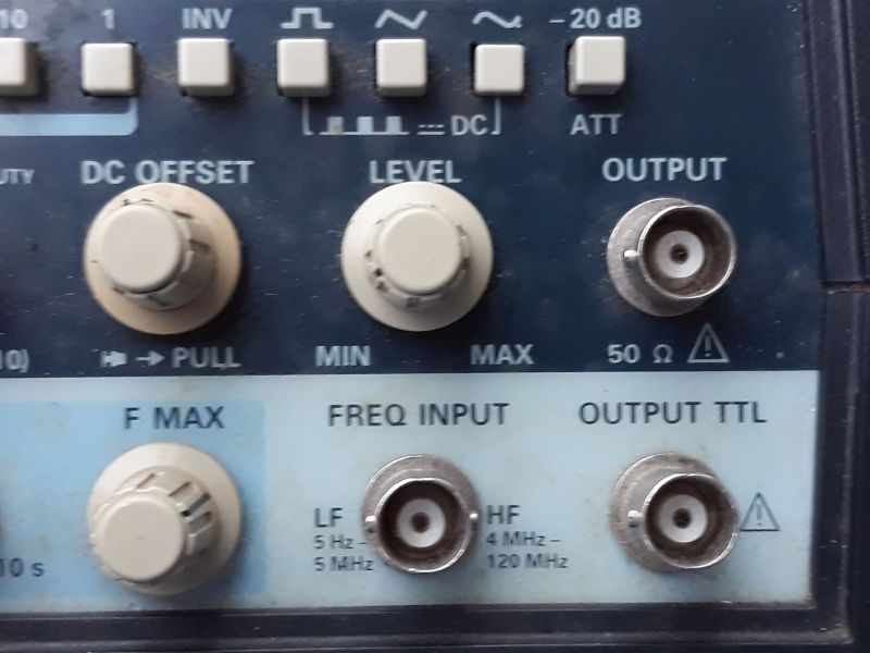 Dieser Alt-Text wurde noch nicht überprüft.
<p>Zusammenfassung: Ausschnitt der Frontplatte eines elektronischen Messgeräts mit mehreren Drehknöpfen und BNC-Buchsen für Ausgang und Frequenzeingang.</p>
<p>Detaillierte Beschreibung: Oben verläuft eine Reihe hellgrauer, quadratischer Tasten mit Symbolen (u. a. Wellenformen) und Beschriftungen wie INV, DC und -20 dB (ATT). Darunter links ein großer, beigefarbener Drehknopf mit der Beschriftung DC OFFSET und dem Hinweis → PULL; in der Mitte ein gleich großer Knopf LEVEL mit Skala von MIN bis MAX. Rechts daneben eine silberne, runde BNC-Buchse mit der Beschriftung OUTPUT und 50 Ω sowie einem Warnsymbol. Im unteren, hellblauen Bereich befindet sich links ein weiterer Drehknopf F MAX. In der Mitte ist eine BNC-Buchse unter der Überschrift FREQ INPUT, umgeben von den Angaben LF 5 Hz–5 MHz und HF 4 MHz–120 MHz. Rechts unten eine weitere BNC-Buchse mit der Beschriftung OUTPUT TTL und einem Warnsymbol. Die Front ist dunkelblau mit hellblauen Feldern; die Bedienelemente wirken leicht benutzt.">
<figcaption>Abbildung NEA-10.2.5: Sinusgenerator mit 50 Ohm Innenwiderstand</figcaption></p>
</figure>
</aside>
<aside class=